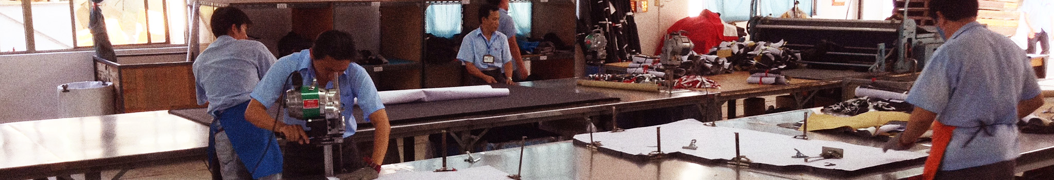 Five factory workers wearing blue shirts cutting material on cutting table