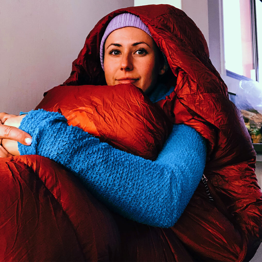 Woman sitting in a red sleeping bag in a cabin, wearing a blue hoody
