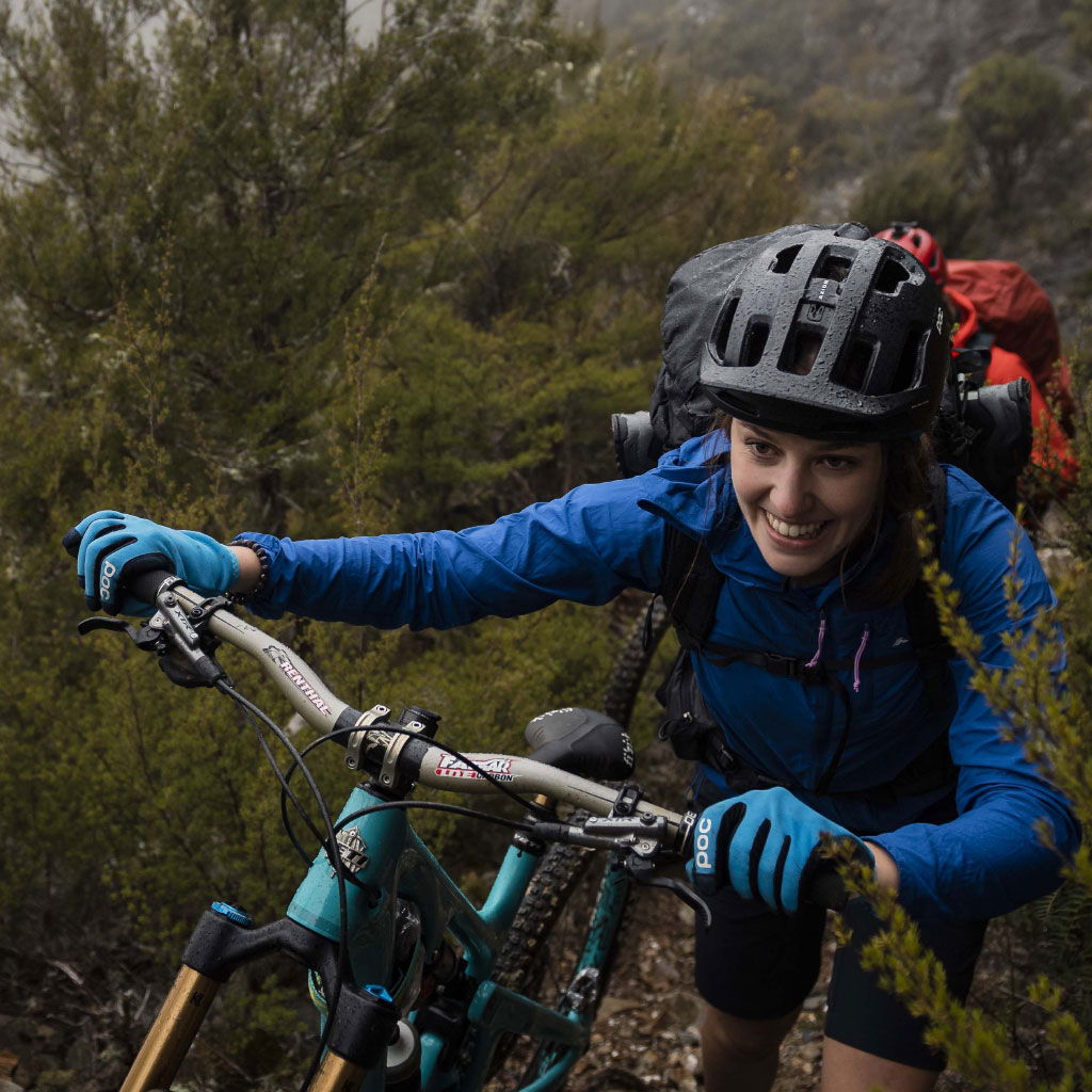Woman pushing bike uphill wearing blue Whitcombe Jacket