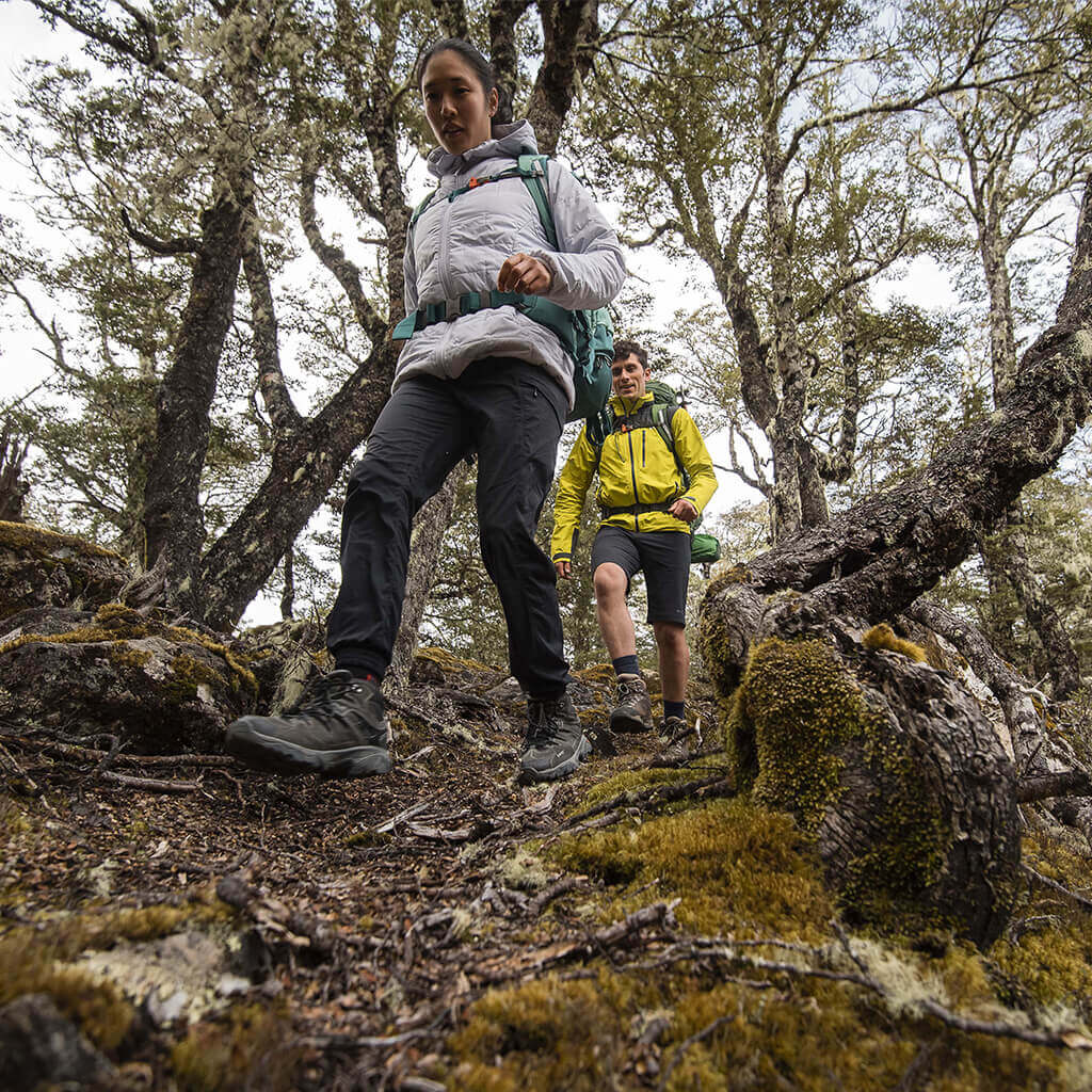 low perspective of 2 people walking through trees wearing hiking boots and rain jackets