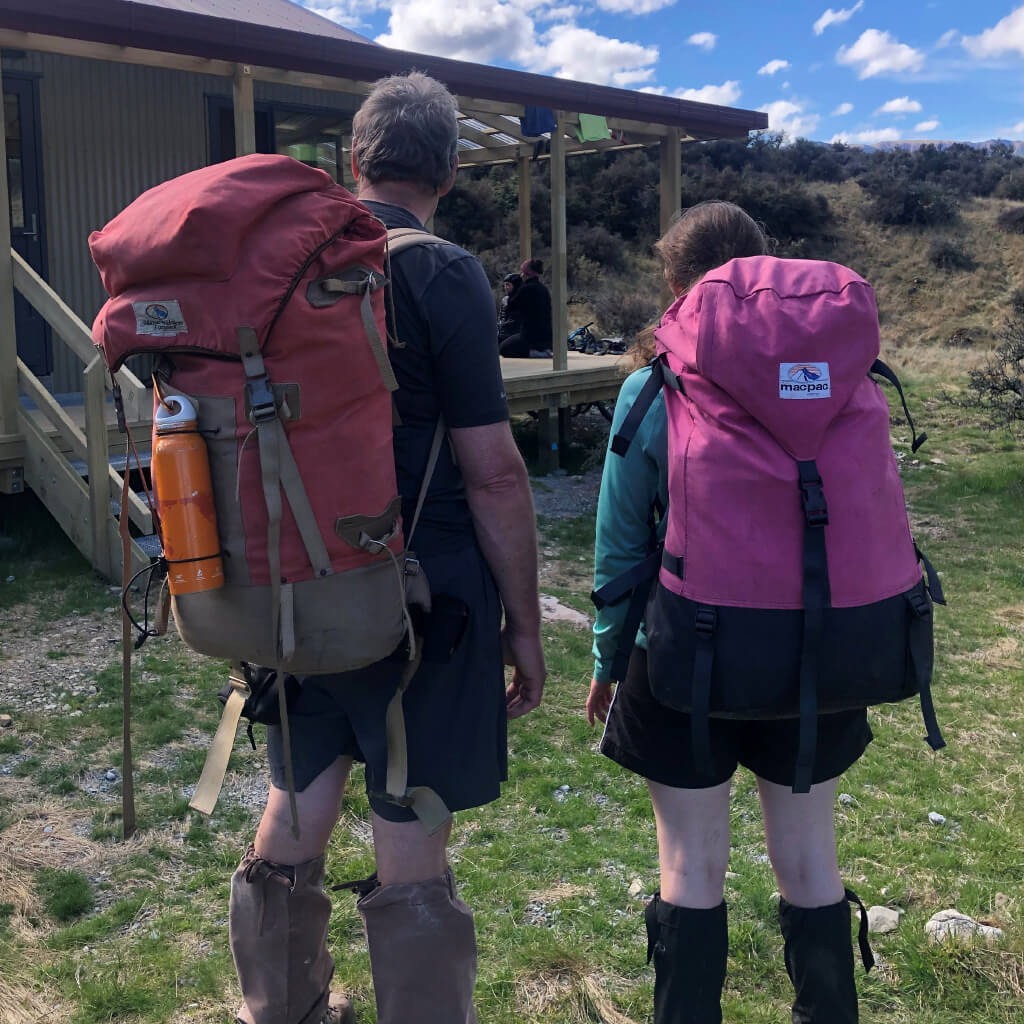 3 people hiking through high country towards a braided river