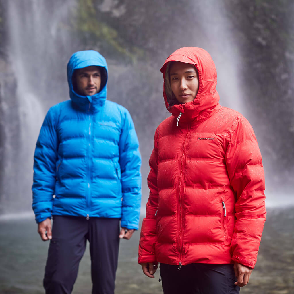 2 people wearing insulated jackets hiking a steep mountain with snow in the background