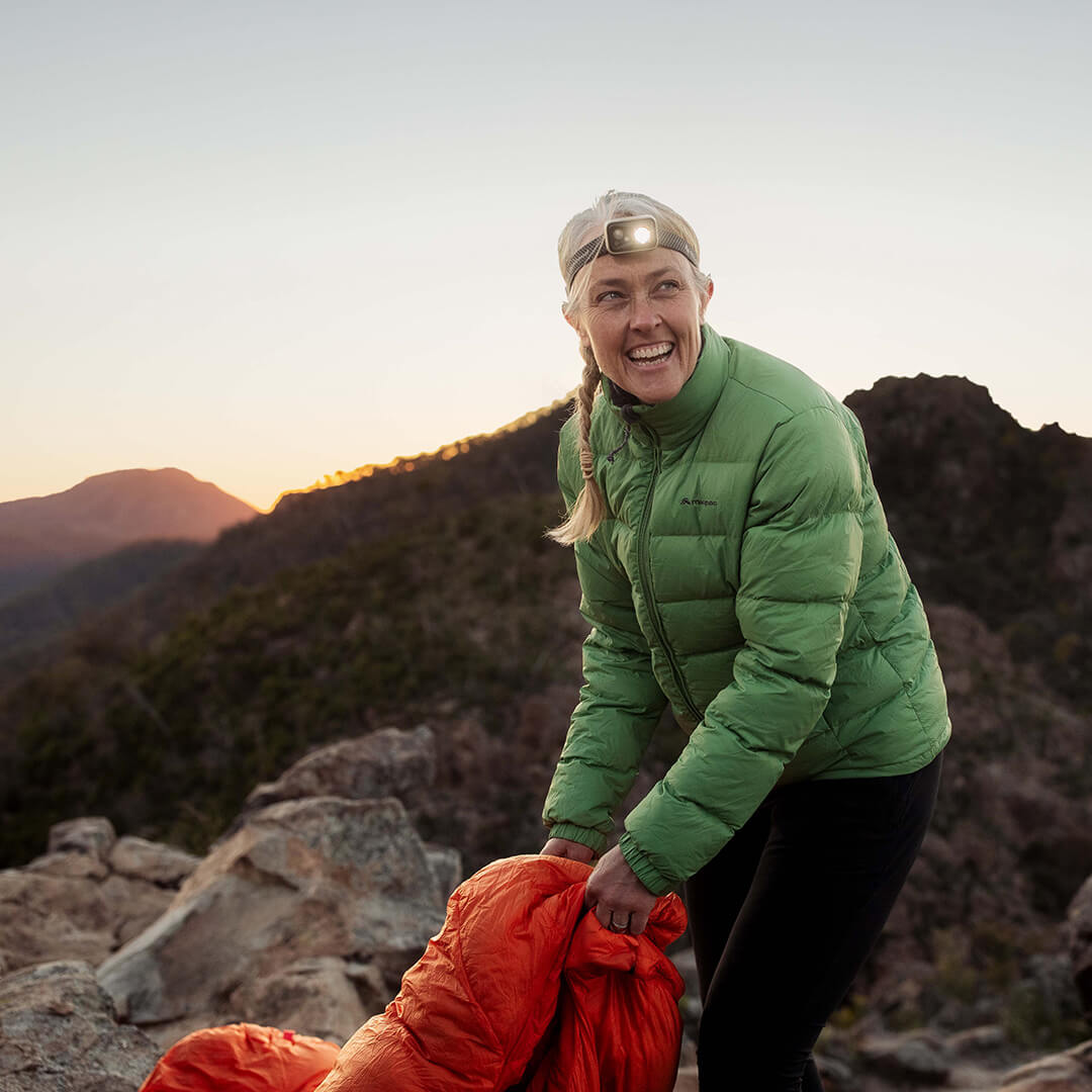 Woman packing away orange sleeping bag at dawn