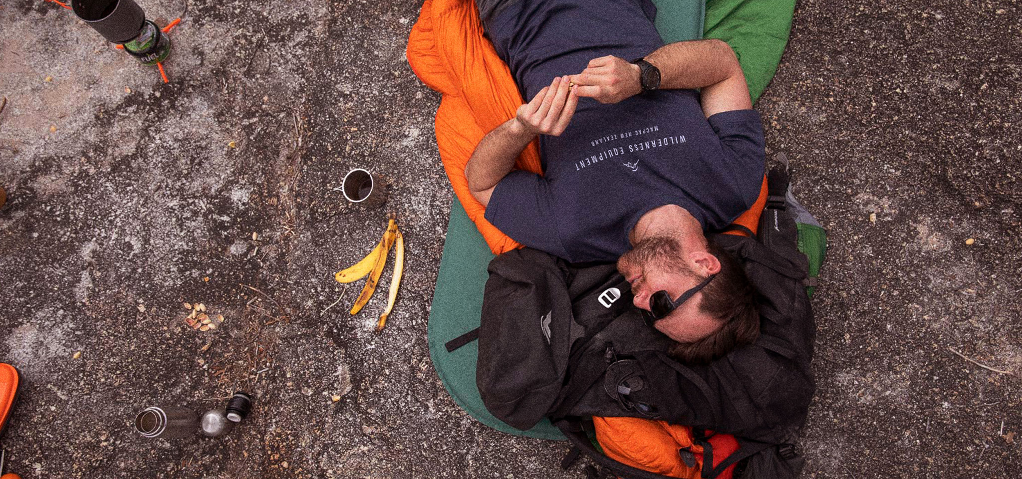 Man Wearing dark blue Macpac Tee Shirt lying on the ground