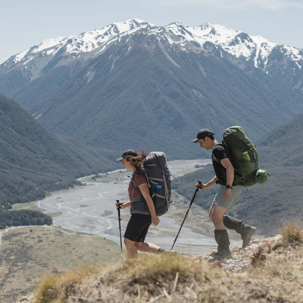 A man and a woman hiking a mountain above a braided river