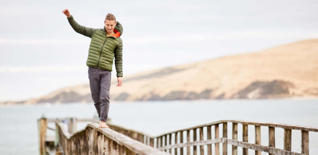 person balancing on wharf wearing green Uber Jacket
