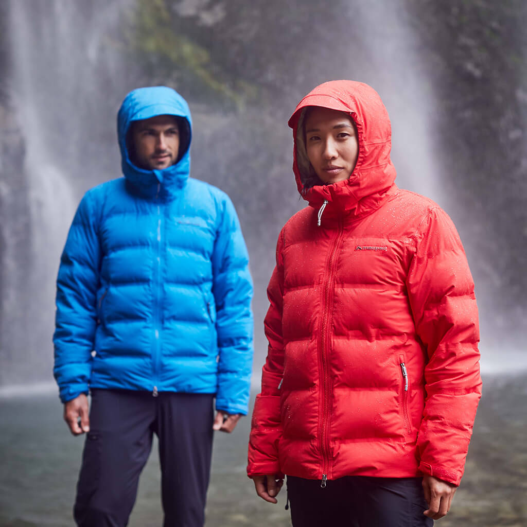 A man and woman wearing blue and red hooded equinox jackets in front of a waterfall