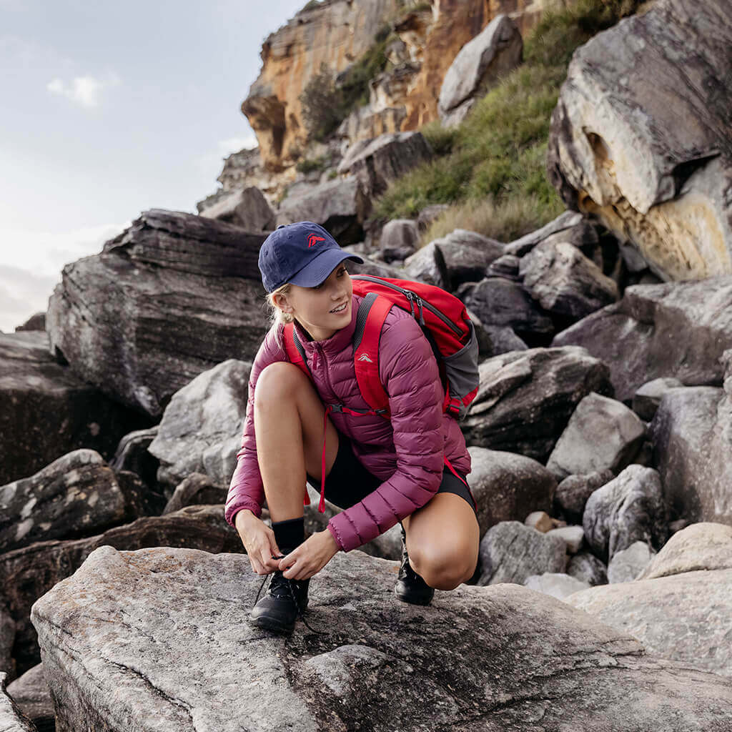 Woman crouching on rock tying up boot lace