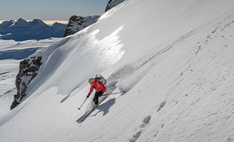 Skier in red jacket carving in sunny snow