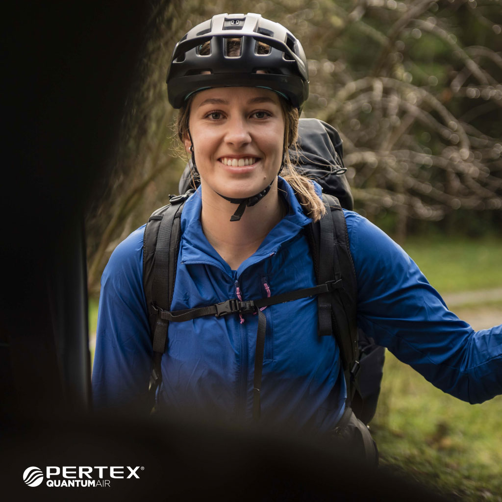 Woman in blue Whitcombe jacket with bike helmet with text Pertex Quatntum Air