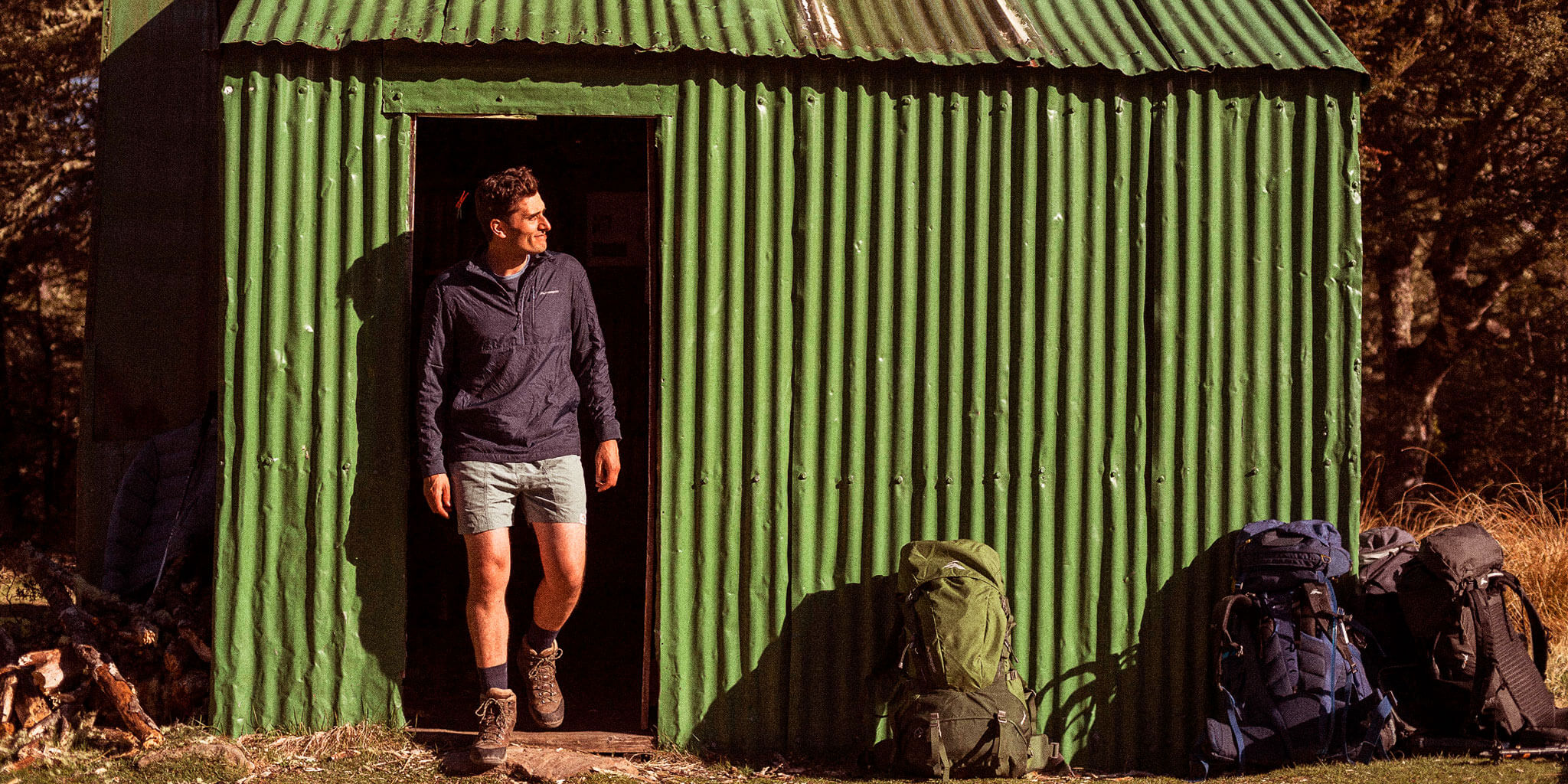 Man wearing macpac apparel standing outside green hut