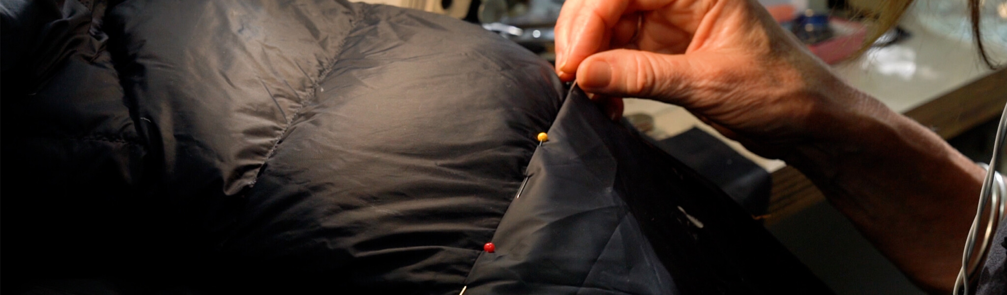 Black down jacket getting repaired with coloured pins threaded in baffle